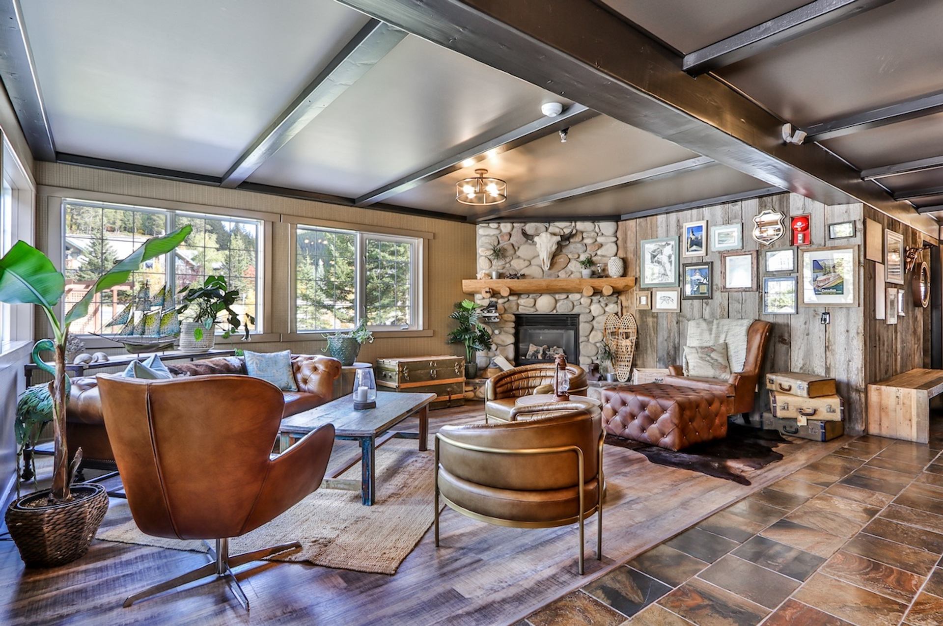 Cozy lounge with leather chairs, stone fireplace, and large windows overlooking trees.