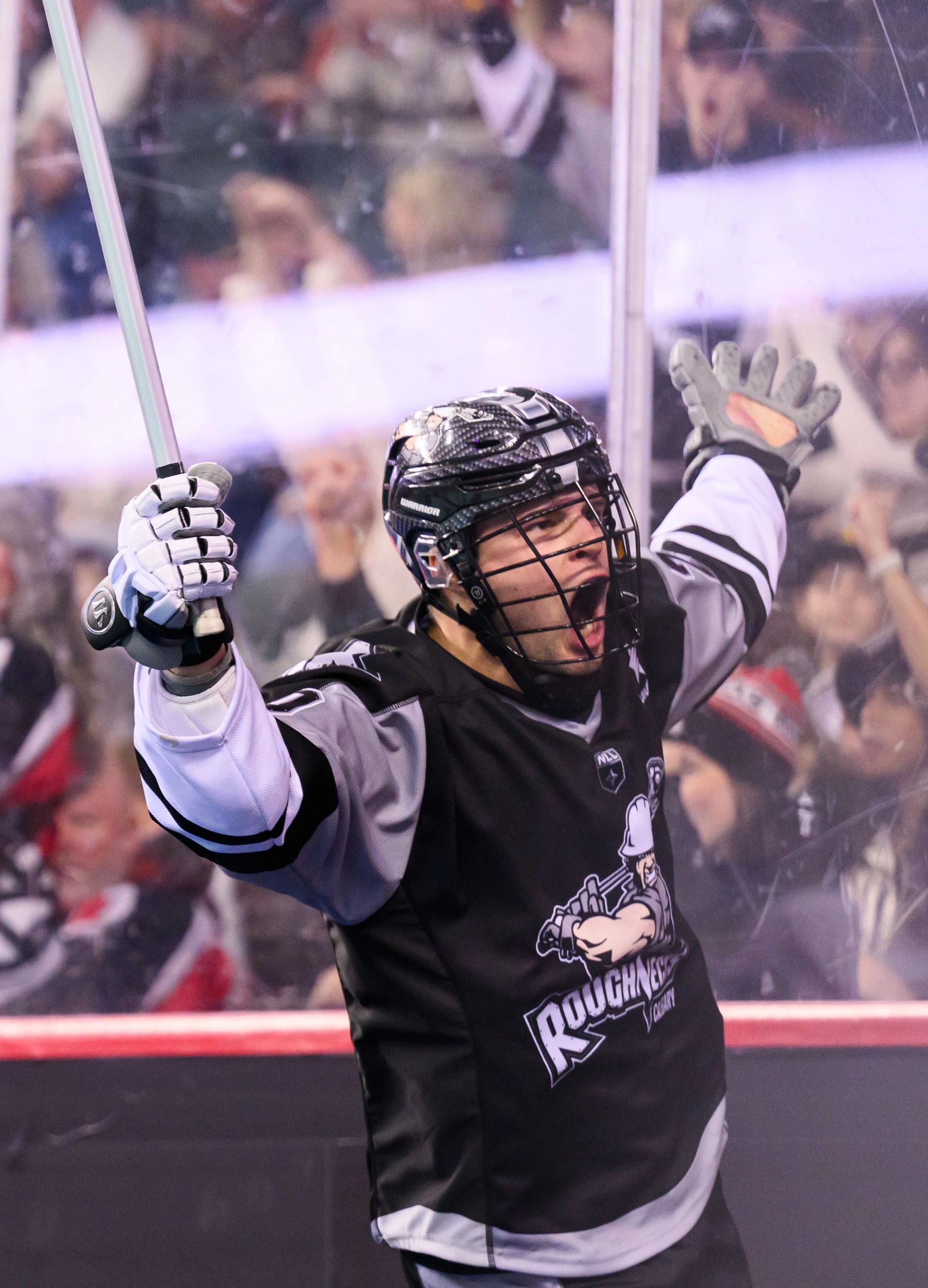 Hockey player in black uniform celebrates on ice with cheering crowd behind glass in arena.
