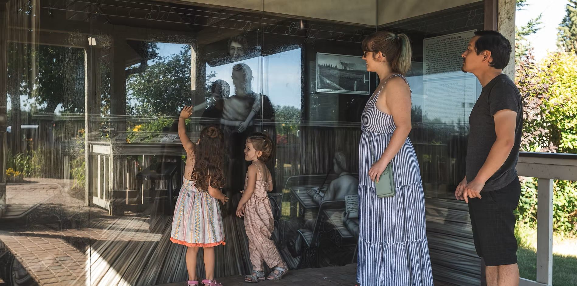 Visitors view historical photographs and displays behind glass at an outdoor exhibit.