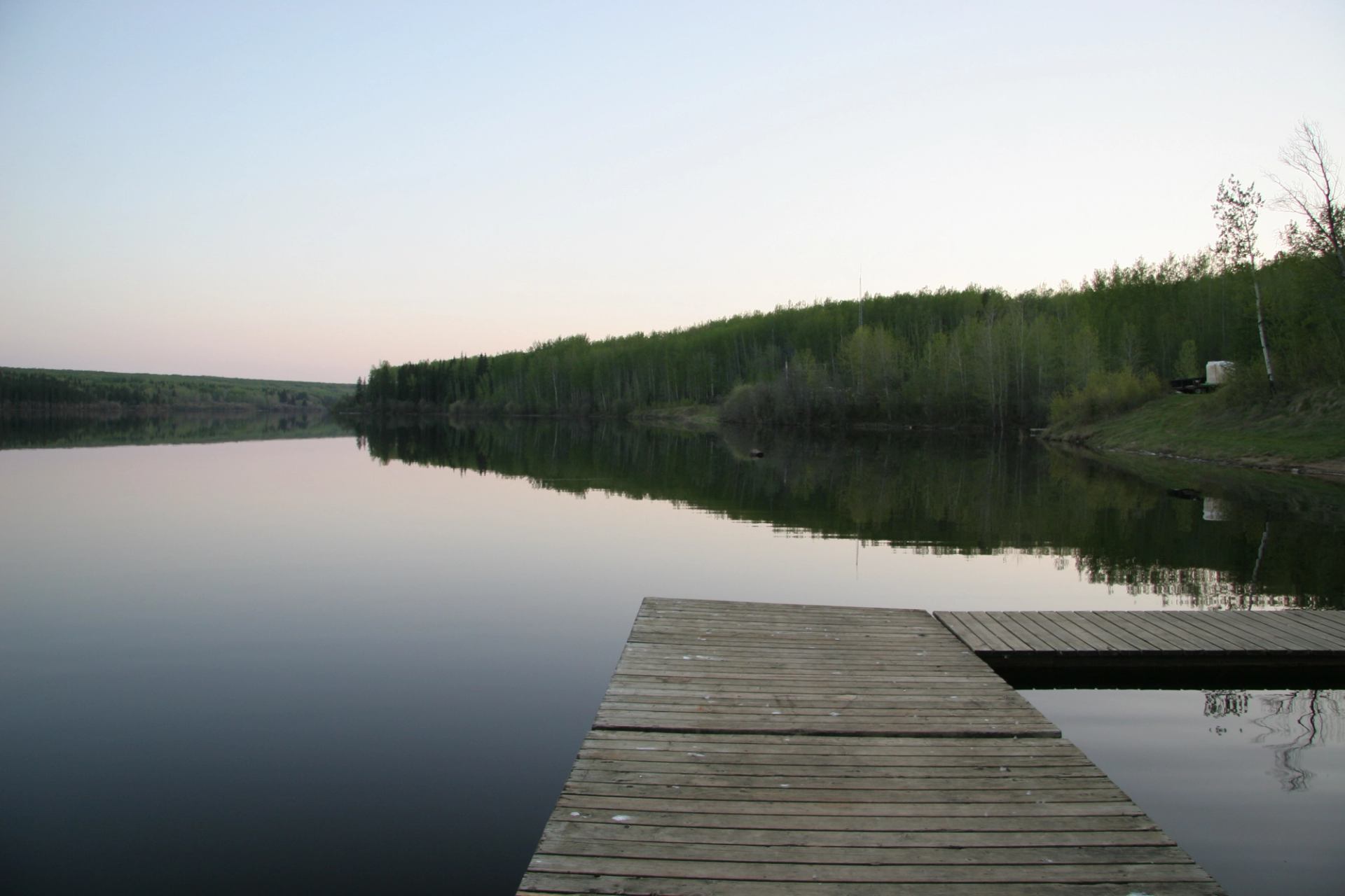 Wooden dock extending over calm lake with tree-covered shoreline reflecting in water.