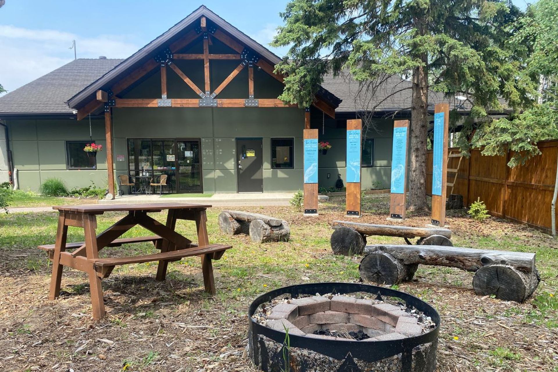 Medicine River Wildlife Centre’s outdoor space with picnic tables, fire pit, benches, and educational signs by a building.