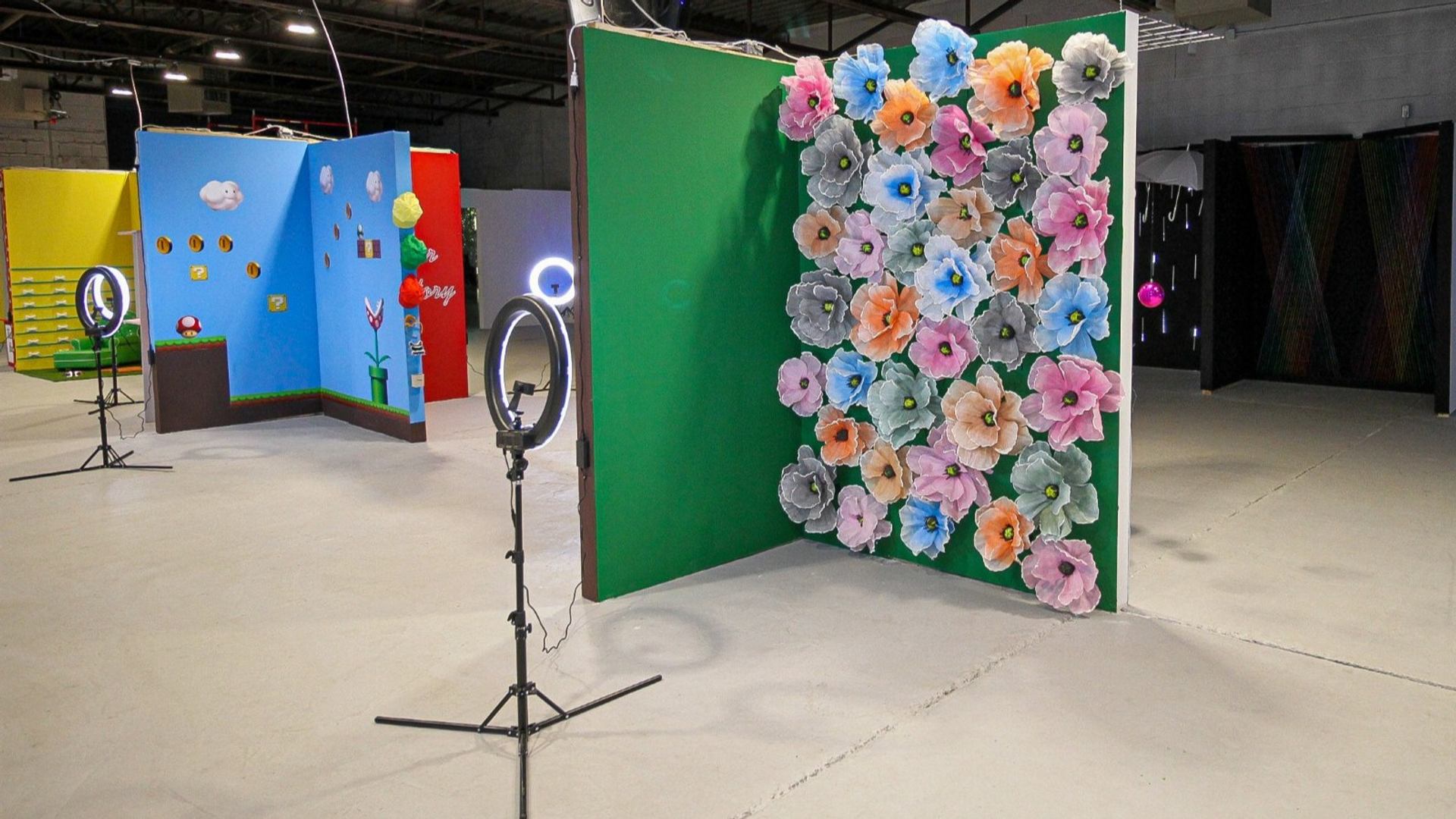 Photo studio with colourful flower wall, themed backdrops and ring lights on stands.