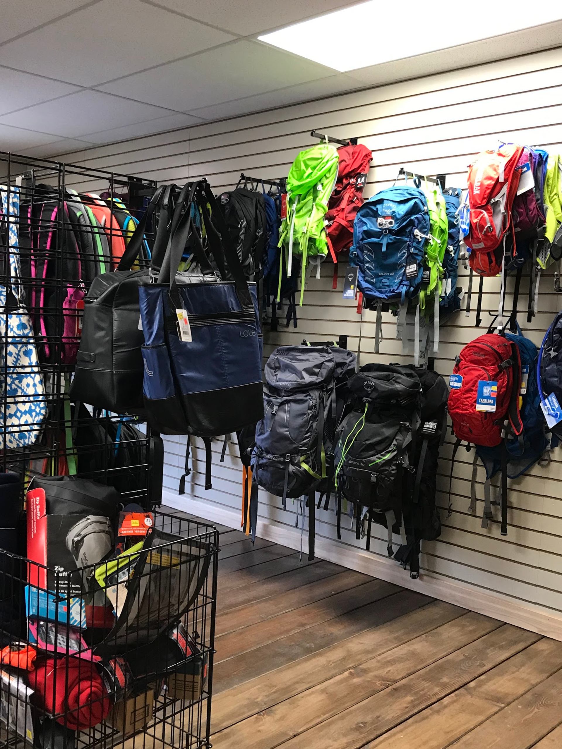 Wall display of colourful hiking backpacks and travel bags in an outdoor gear store.