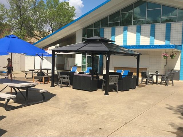 Patio with tables and chairs beside Eastglen Leisure Centre building with blue awnings.