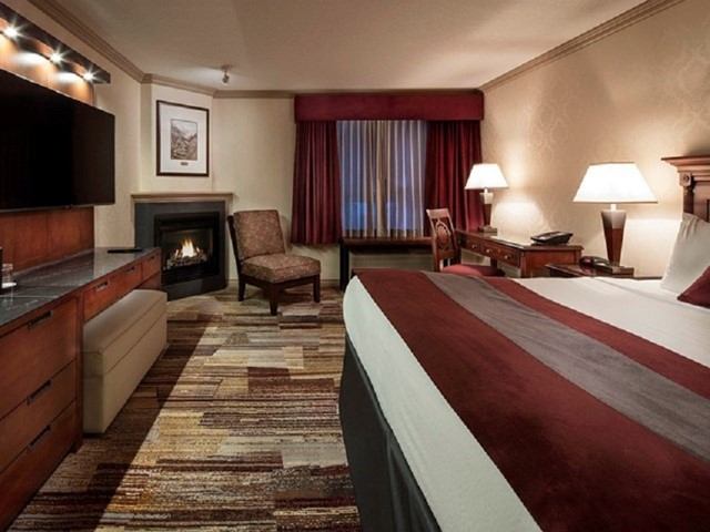 Hotel room with bed, fireplace, TV, desk, chair, and curtained window.