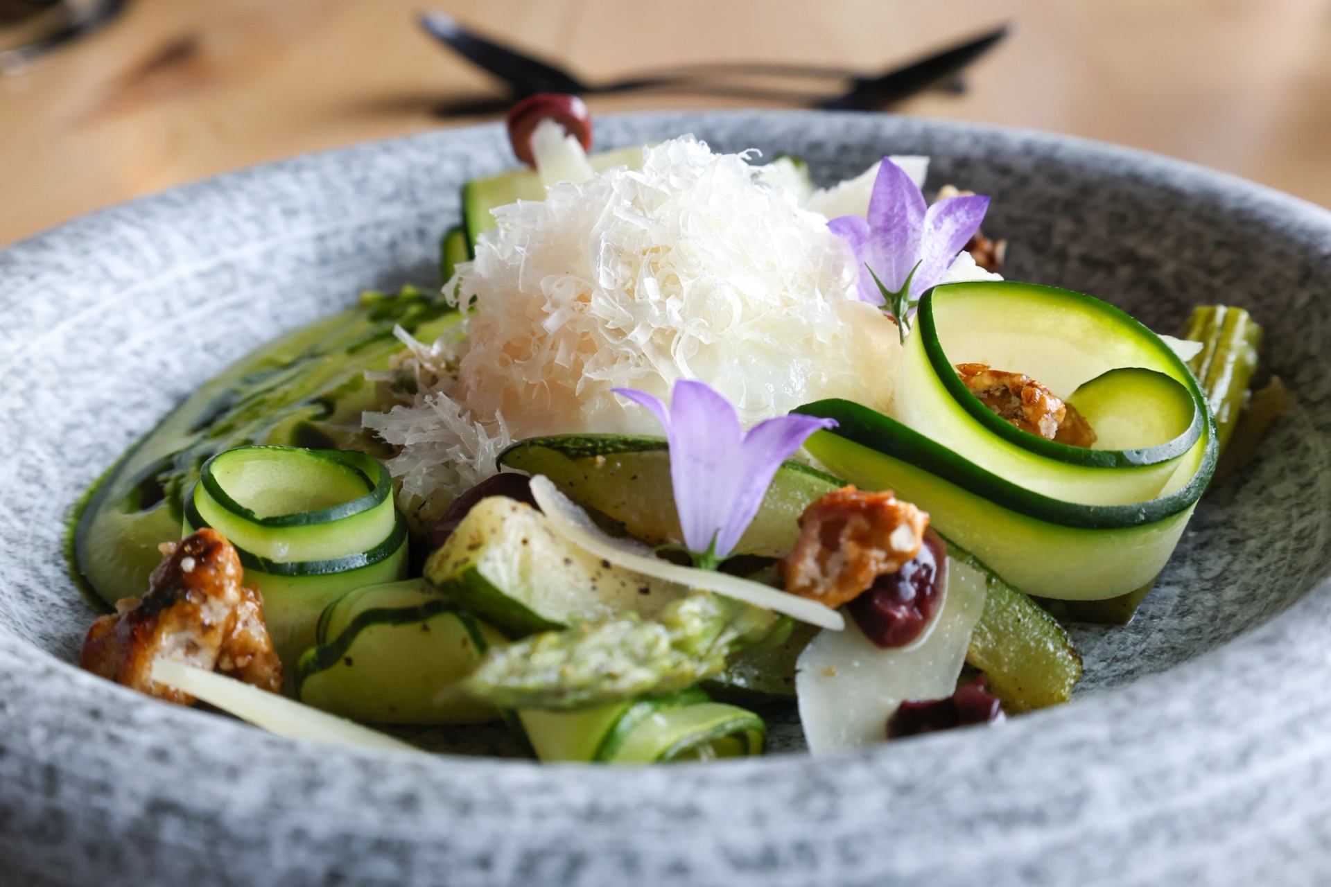 Elegant zucchini ribbon salad with cheese and edible flowers in a gray bowl.
