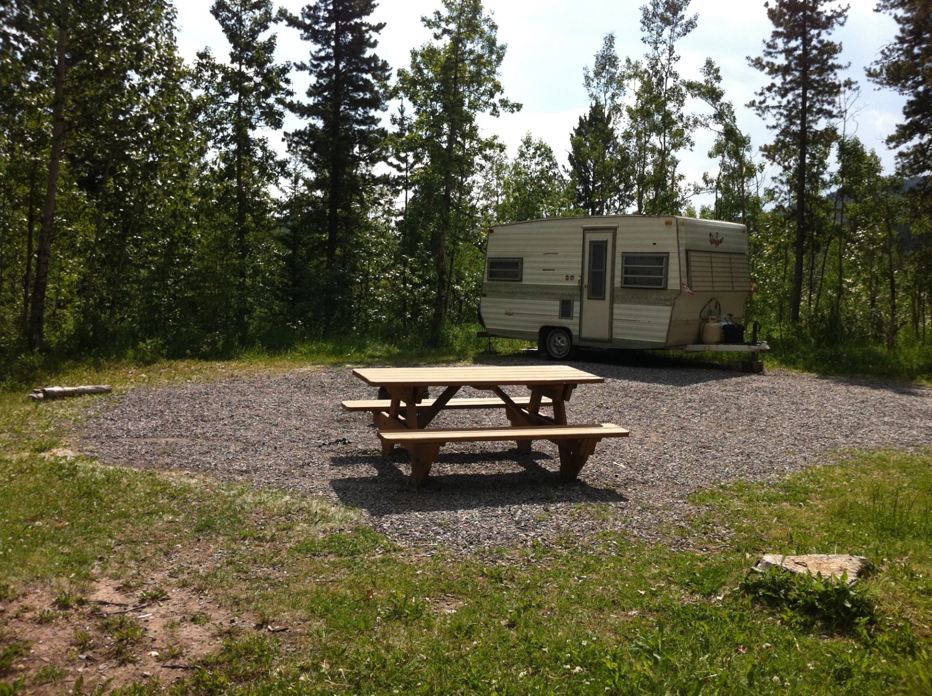 Paddy’s Flat Campground shows a small RV trailer parked on a gravel site with a picnic table, surrounded by tall trees.