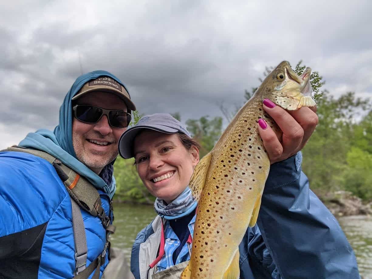 Smiling man and woman holding a large brown trout.