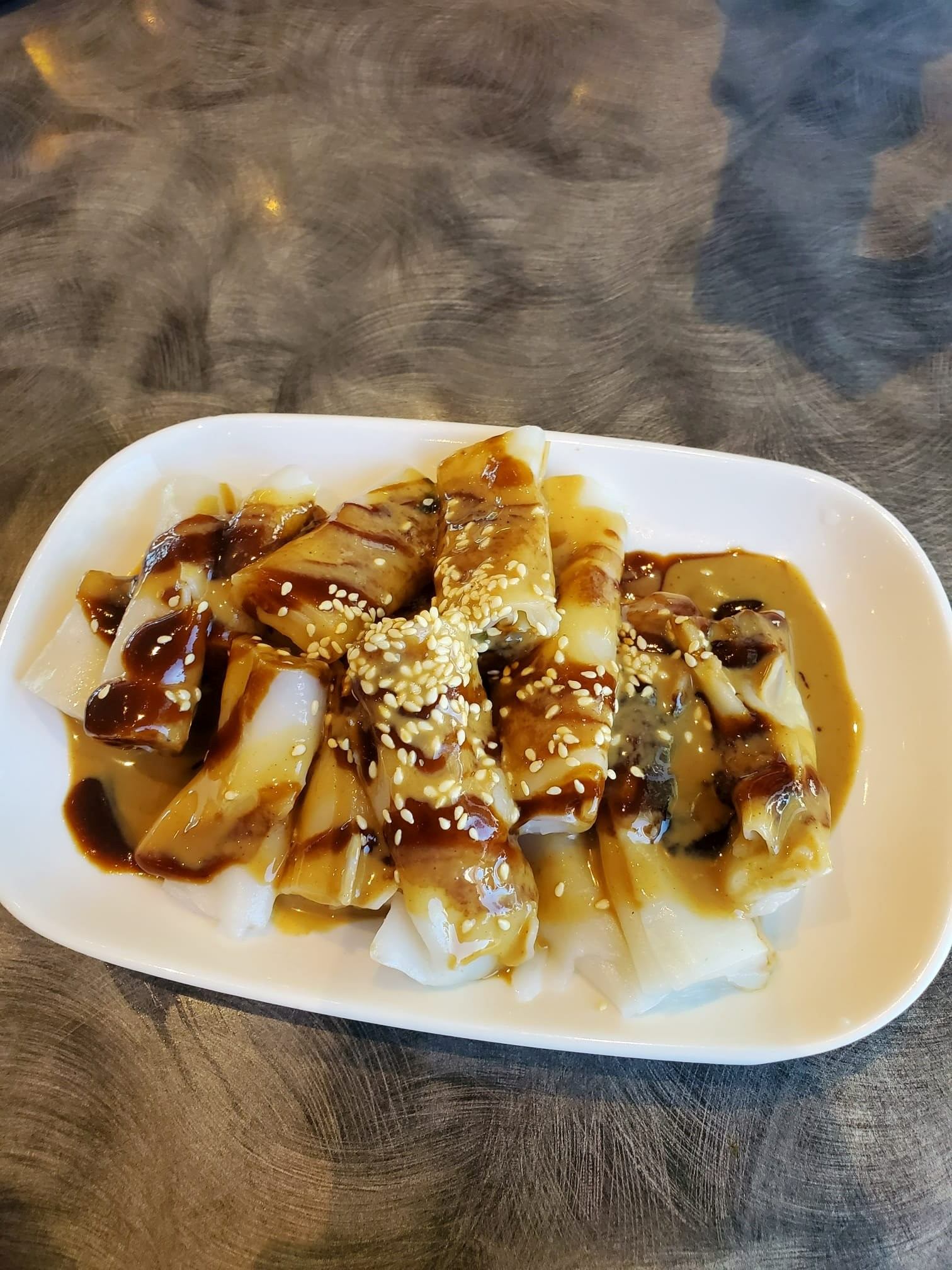 Plate of noodles with sauce and sesame seeds on a wooden table.
