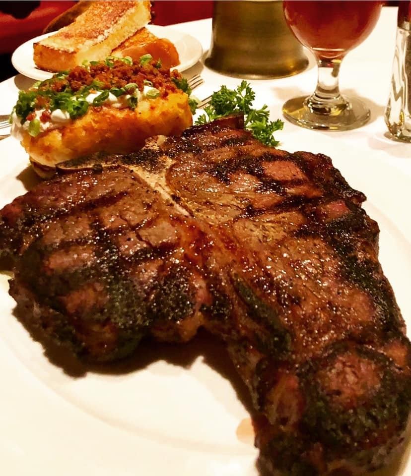 Grilled steak with baked potato, toast and drinks on a white tablecloth.