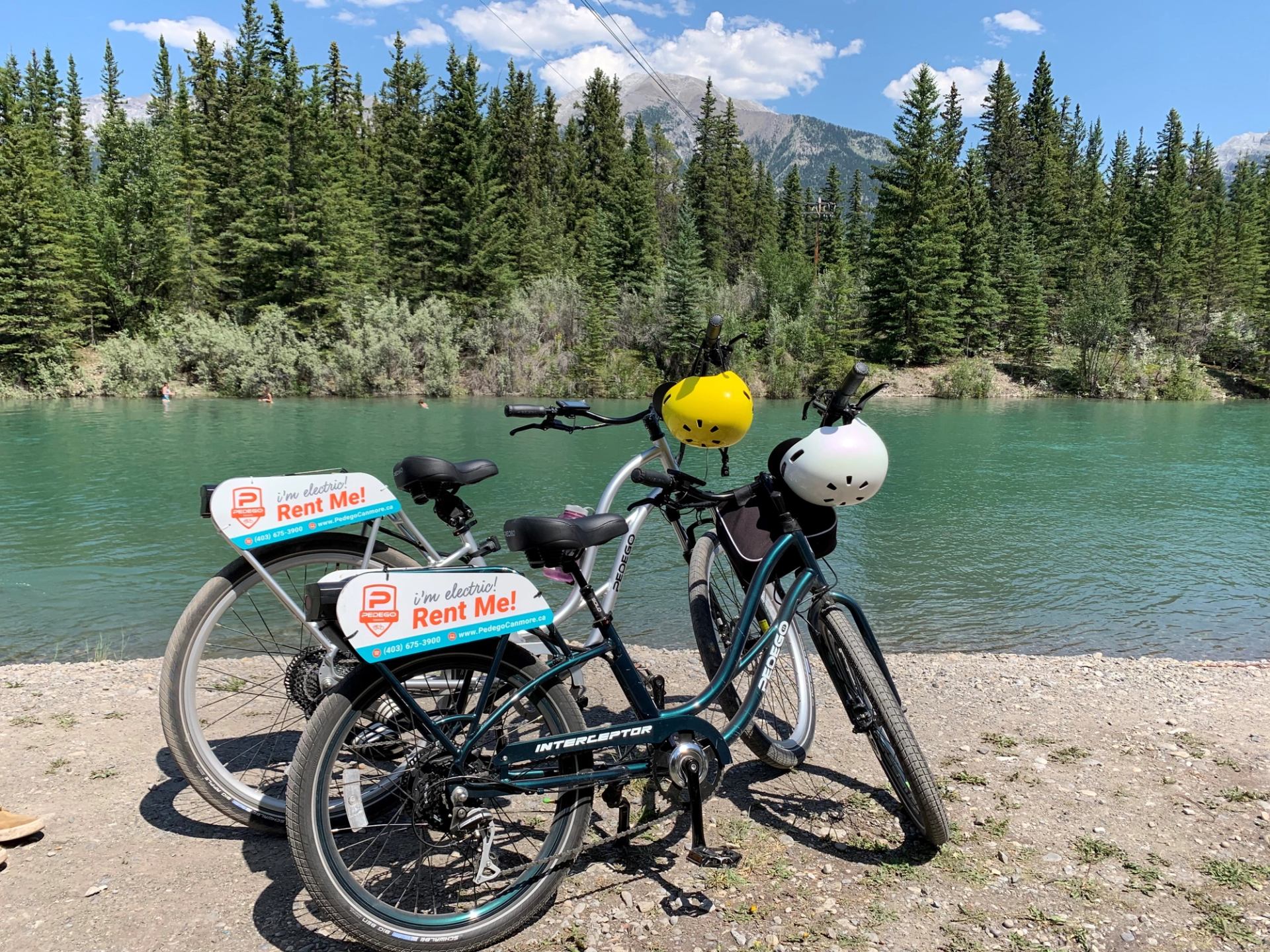 Two rental bikes parked by water with forest and mountain views.
