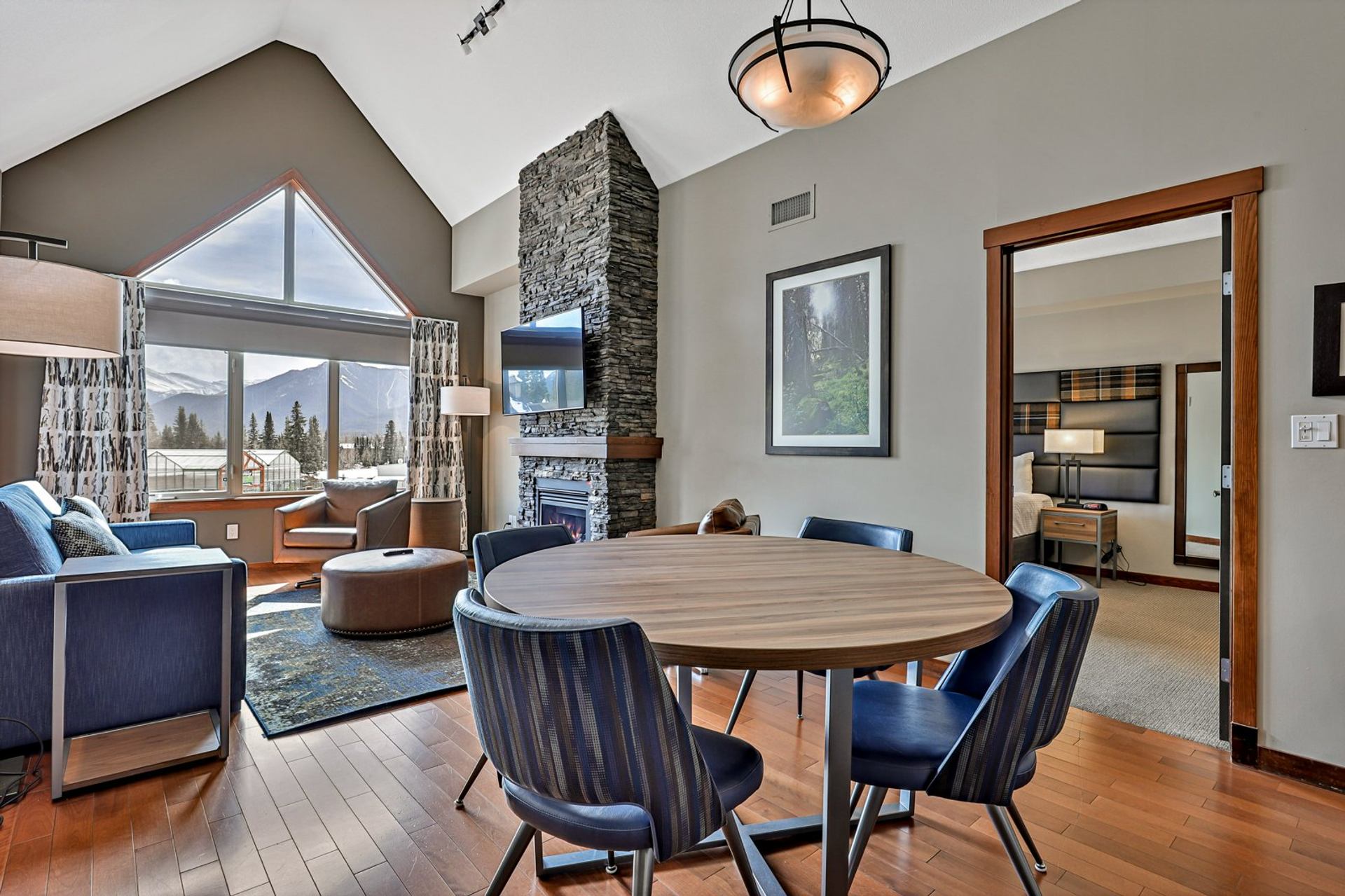 Open living and dining area with stone fireplace, round table and mountain view.