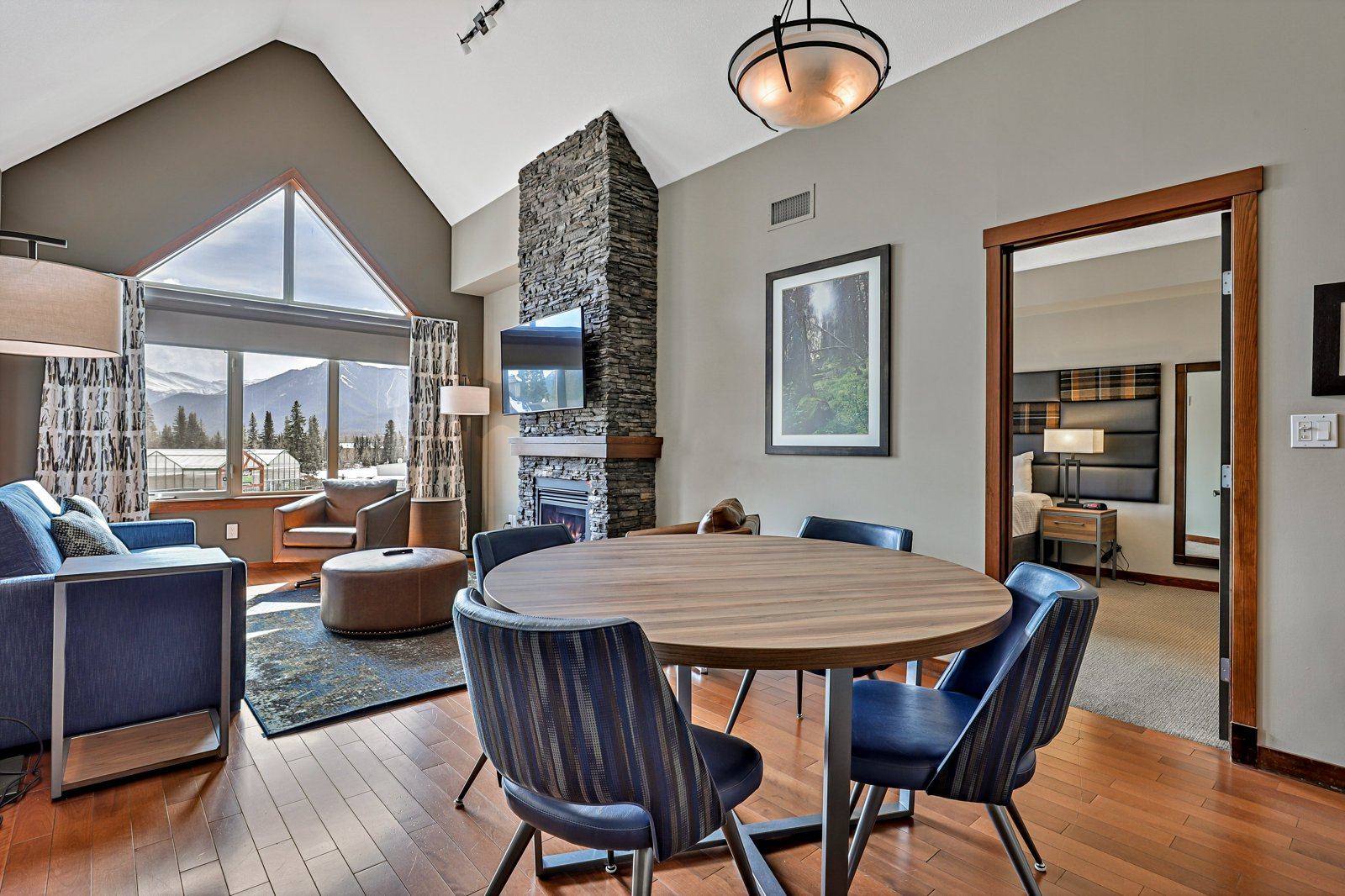 Open living and dining area with stone fireplace, round table and mountain view.