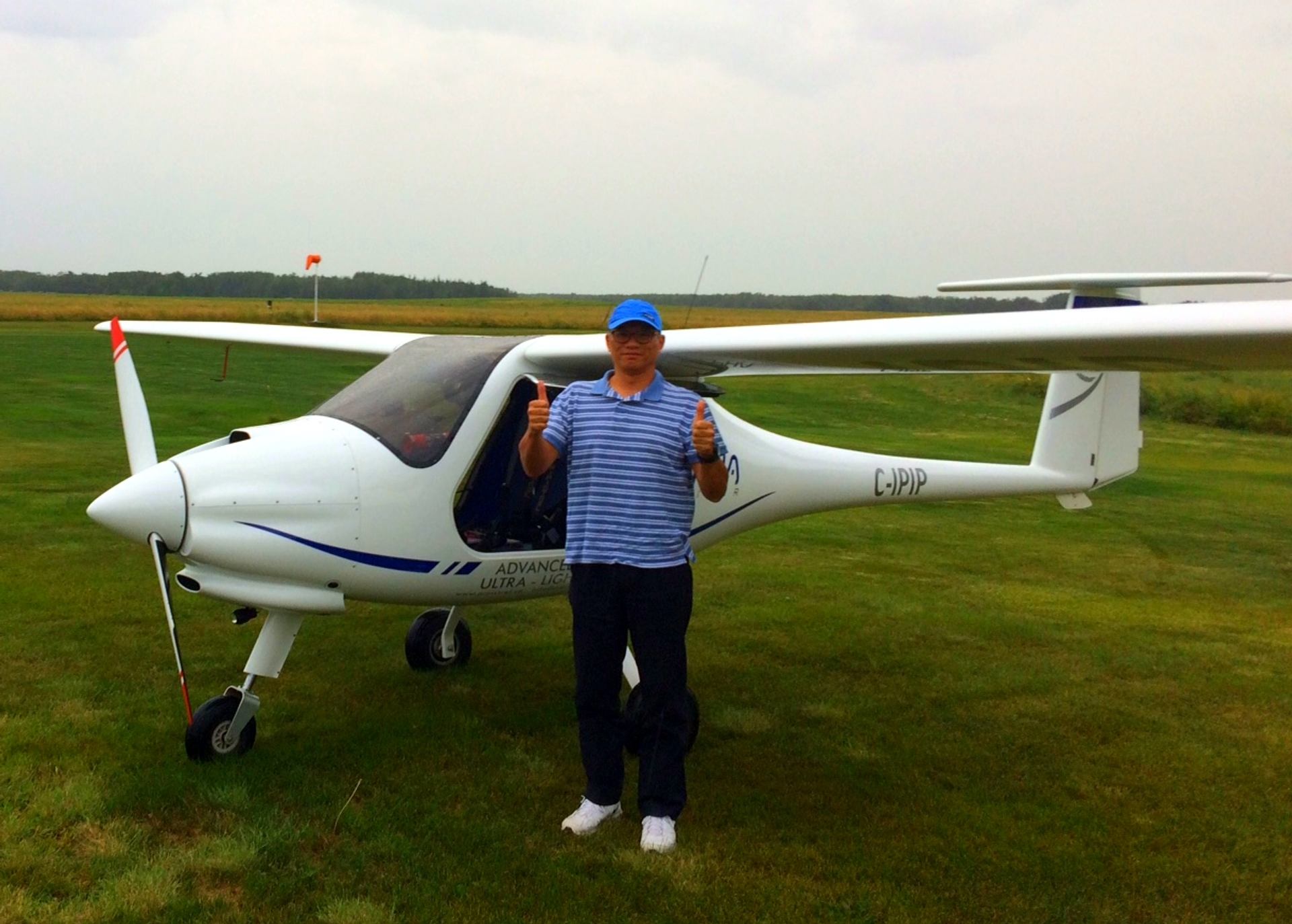 Person standing beside a sleek white ultralight aircraft on a grassy airfield.