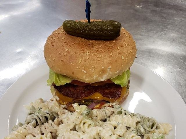 Burger with bacon, cheese, and pickle, served with creamy pasta salad.