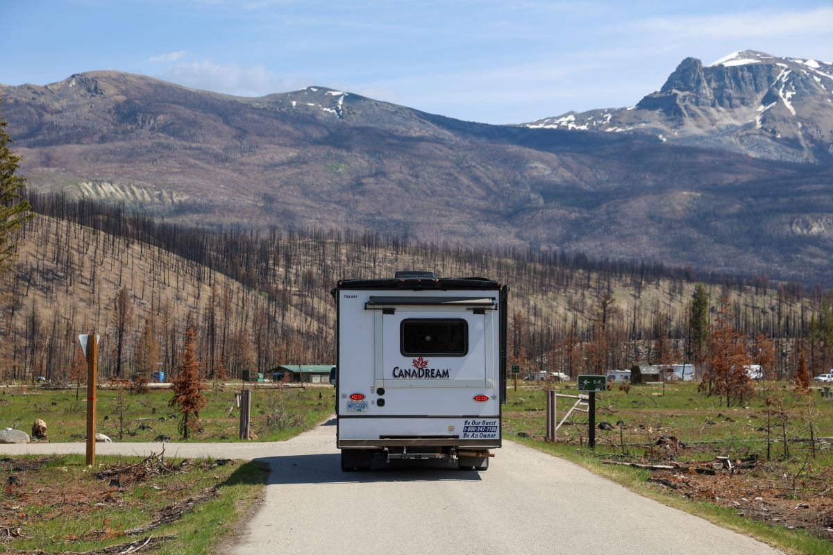 Recreational vehicle with CanaDream logo drives on paved road toward mountain range.