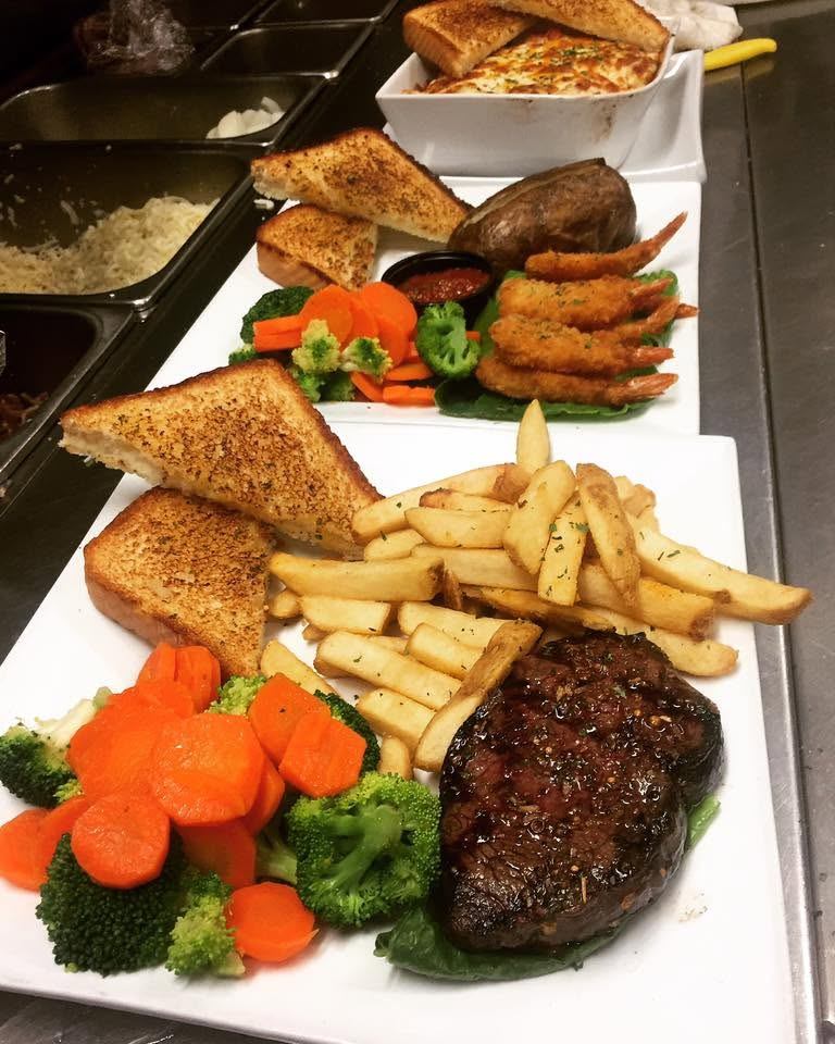 Steak, fries, vegetables, shrimp, baked potatoes, and toast are plated and ready to be served.