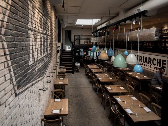 Model Milk interior with wooden tables, colorful lights, and a mural on a brick wall.