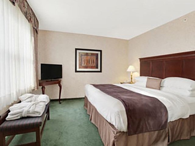 Hotel room with two beds, lamp, television, and framed wall art on beige walls.