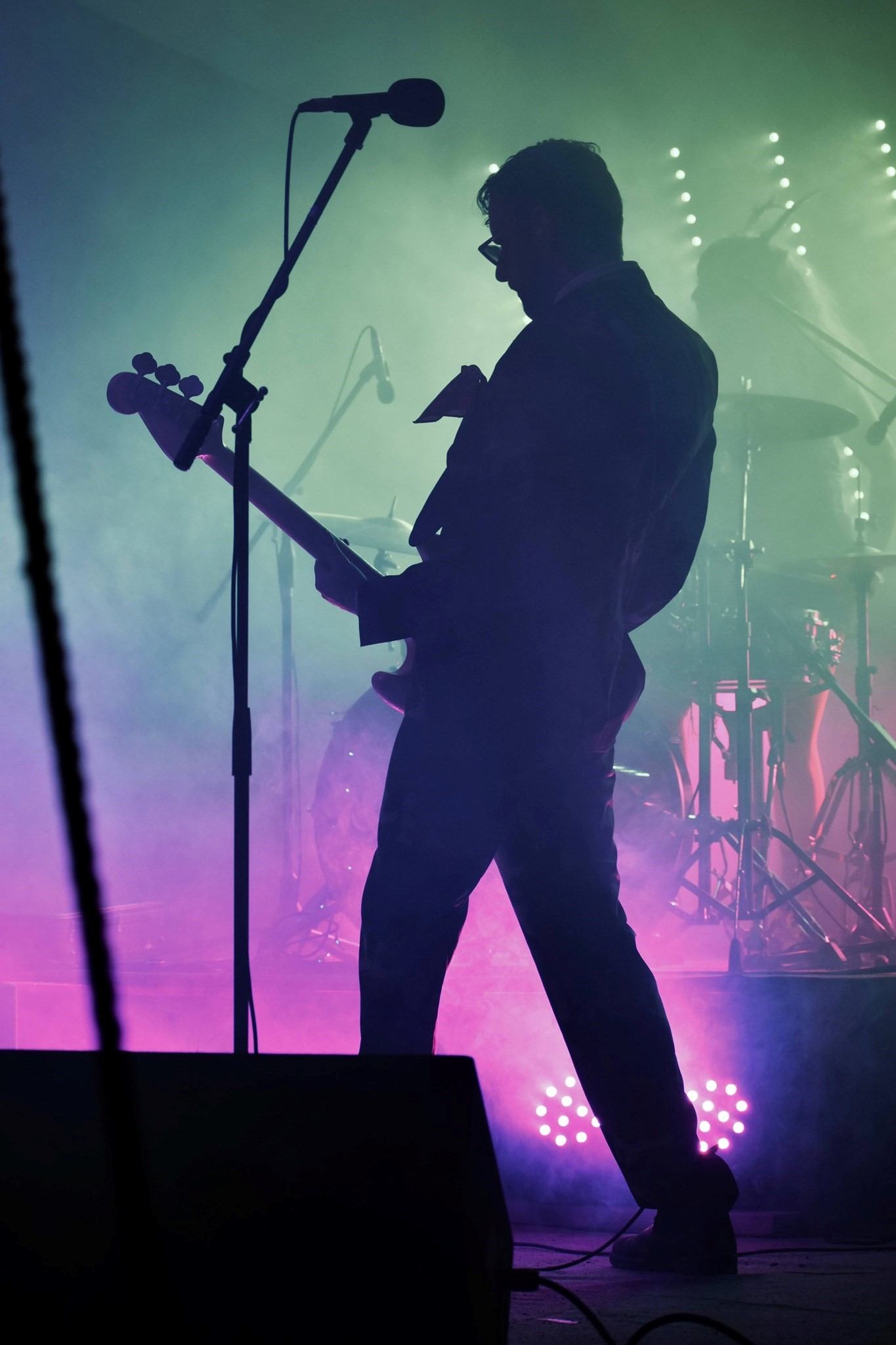 Guitarist silhouette performing on stage with microphone and stage lights at a music festival.