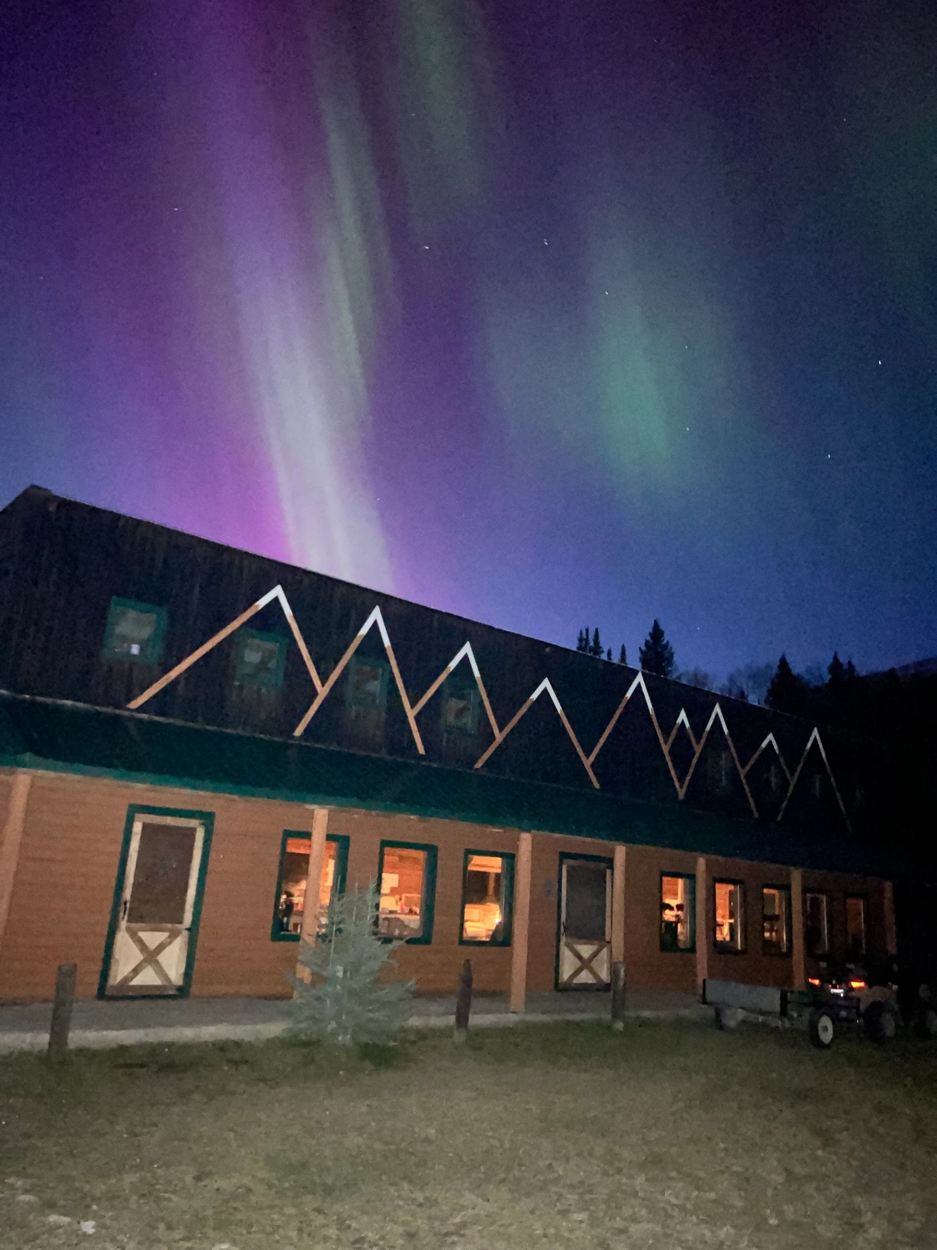 Aurora borealis glowing above ranch buildings at night.