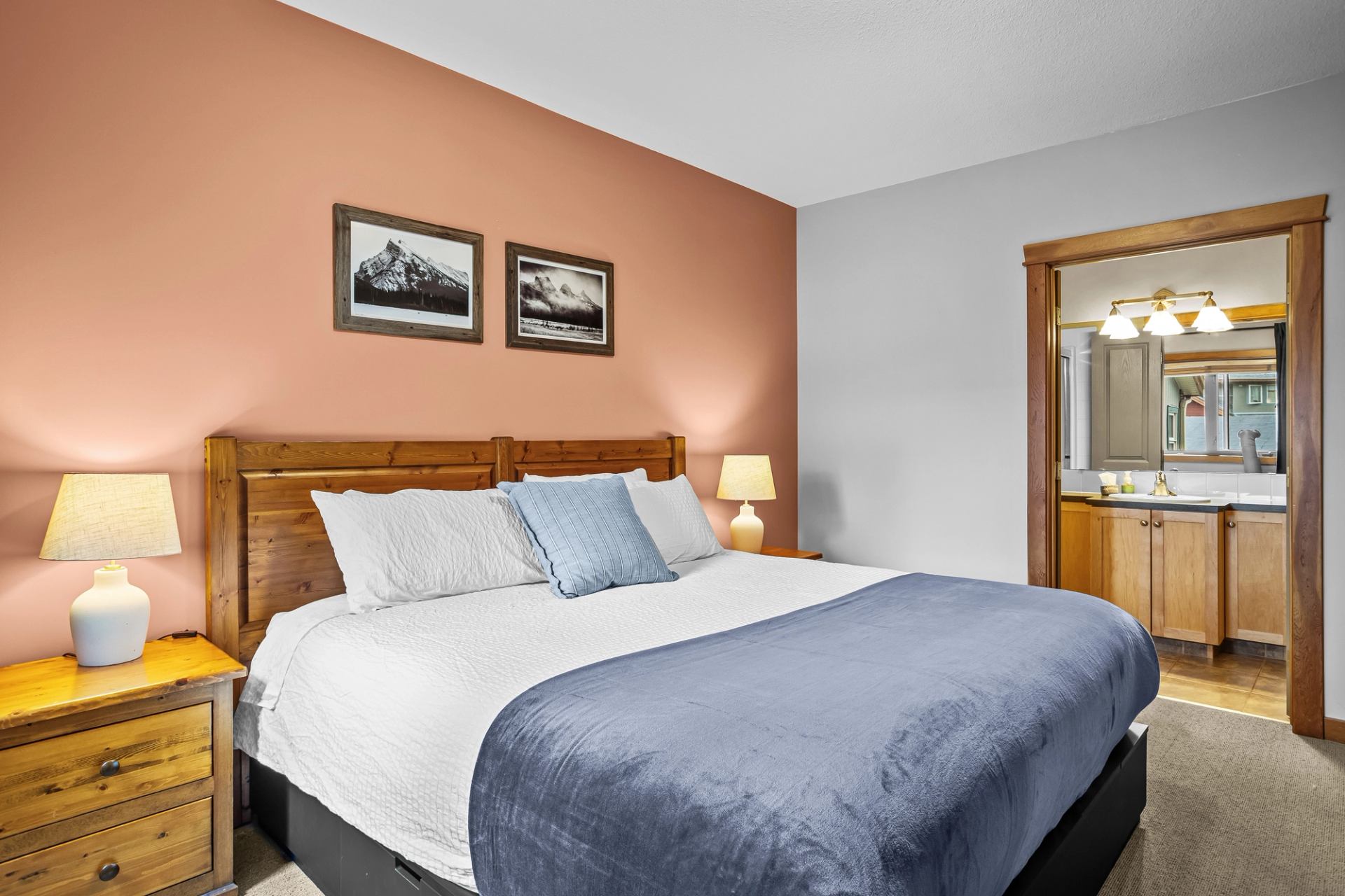 Bedroom with wooden bed, blue blanket, bedside lamps and adjoining bathroom.