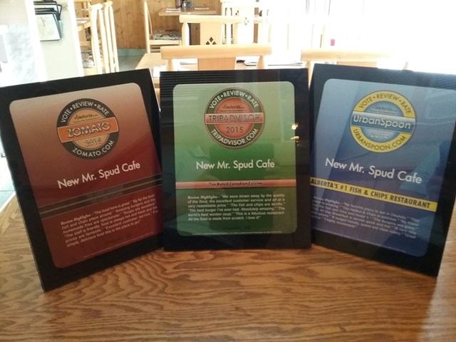 Three framed awards displayed on a wooden table at The New Mr. Spud Café