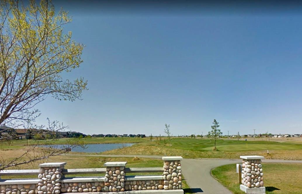 Open fairway with a pond and trees seen from a stone fence under a clear blue sky