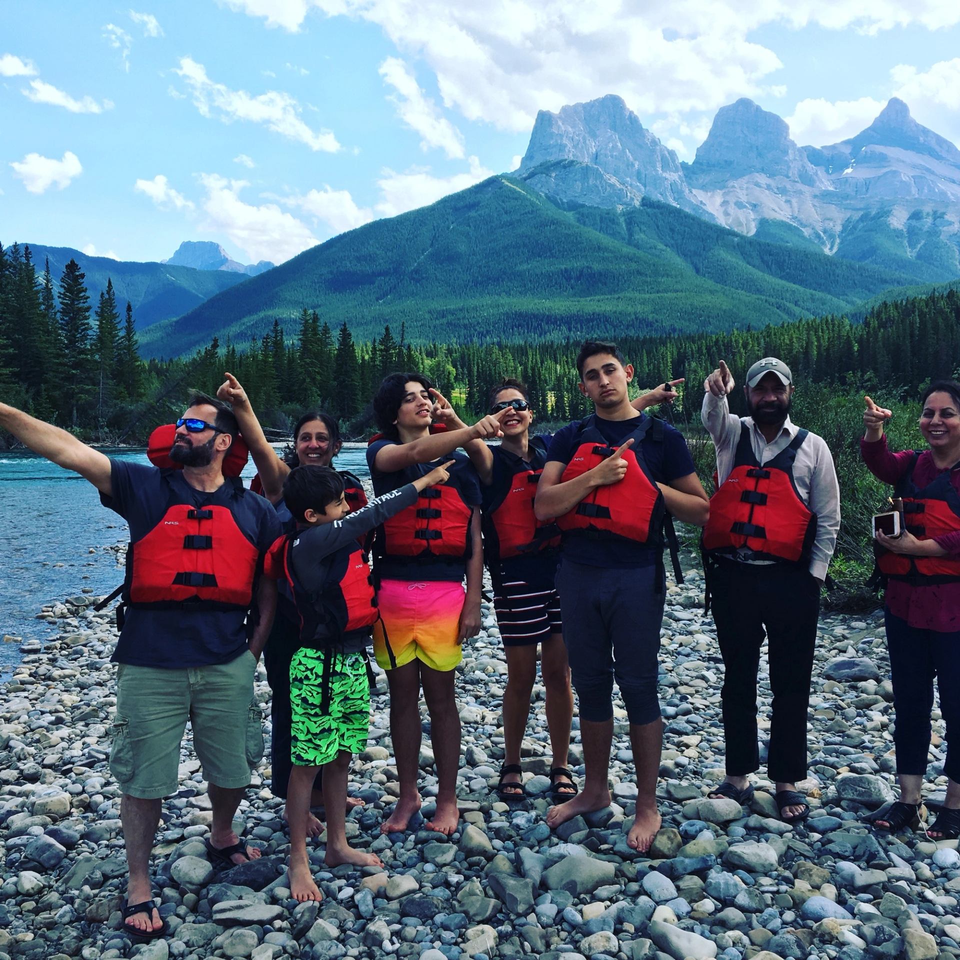 Group in life jackets on rocky riverbank with mountain backdrop.