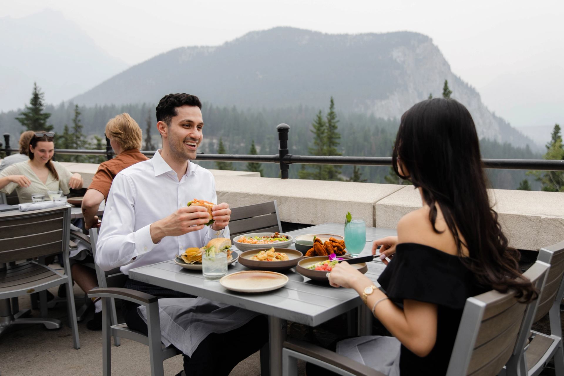 Outdoor dining at The Rundle Patio with plates of food and mountain views in the background.
