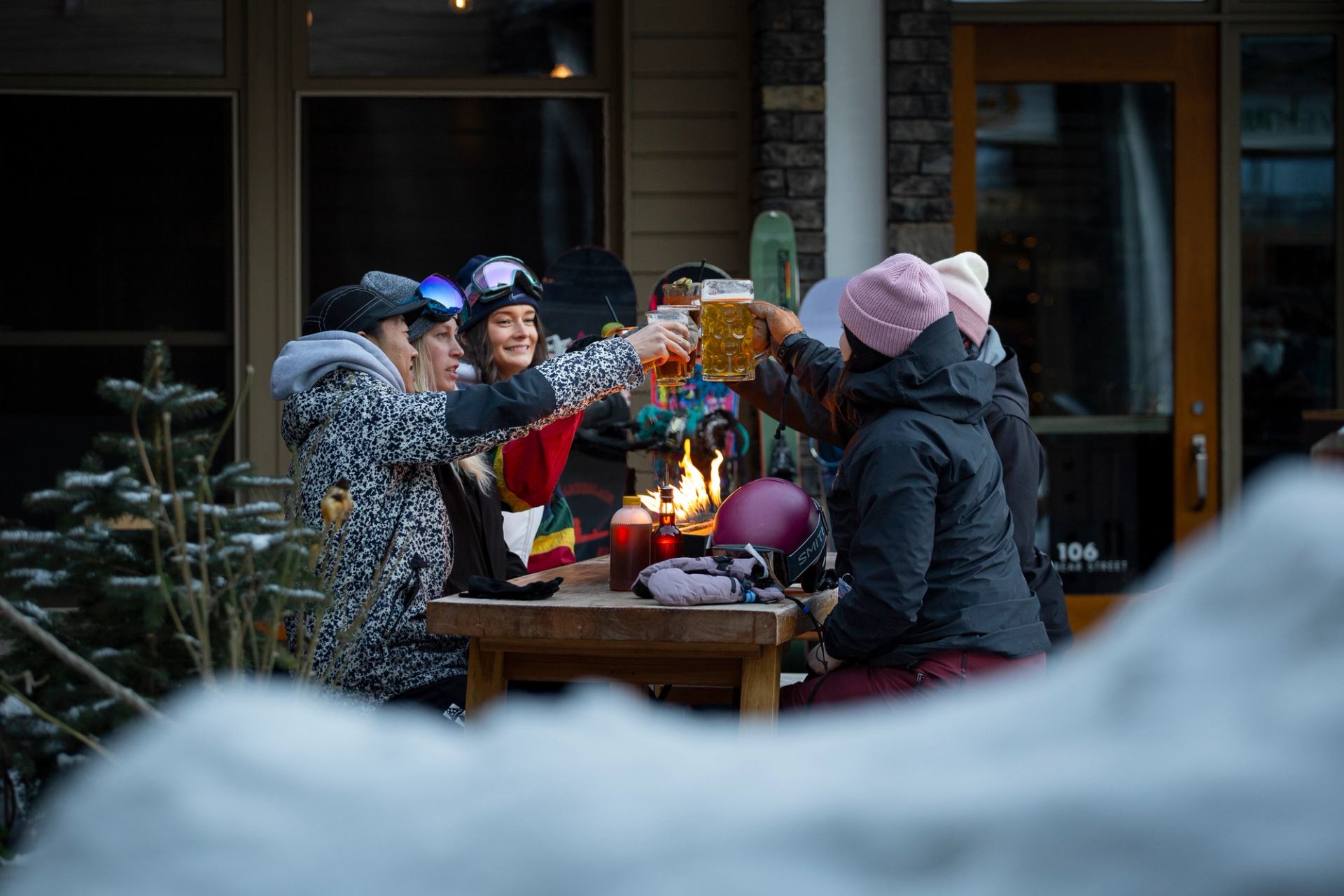 A group of skiers cheers their glasses in front of the fire on the courtyard patio.