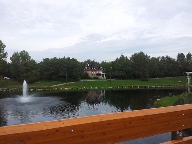 Cronquist House with pond fountain and greenery viewed from wooden bridge.