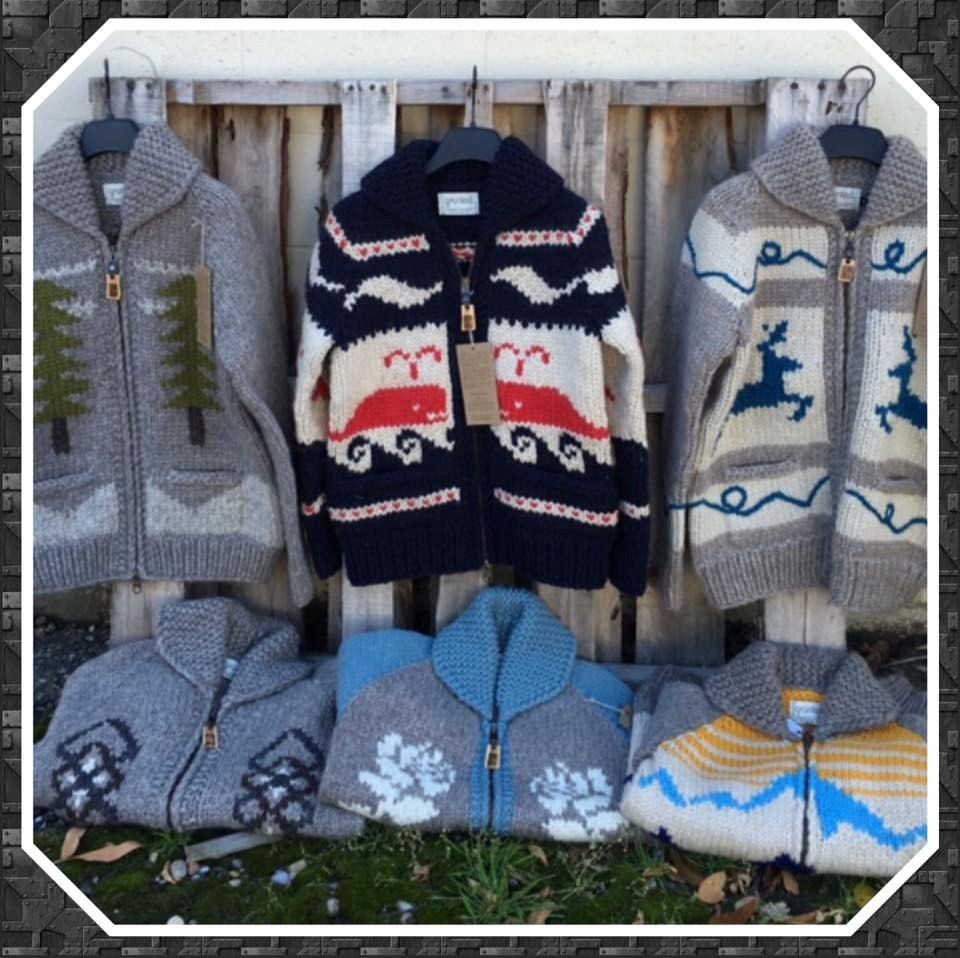Knitted zip-up sweaters on display with trees and animal patterns on wooden hangers.