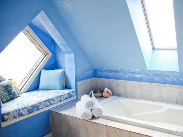 Cozy blue bathroom with soaking tub, window seat, and soft natural light.