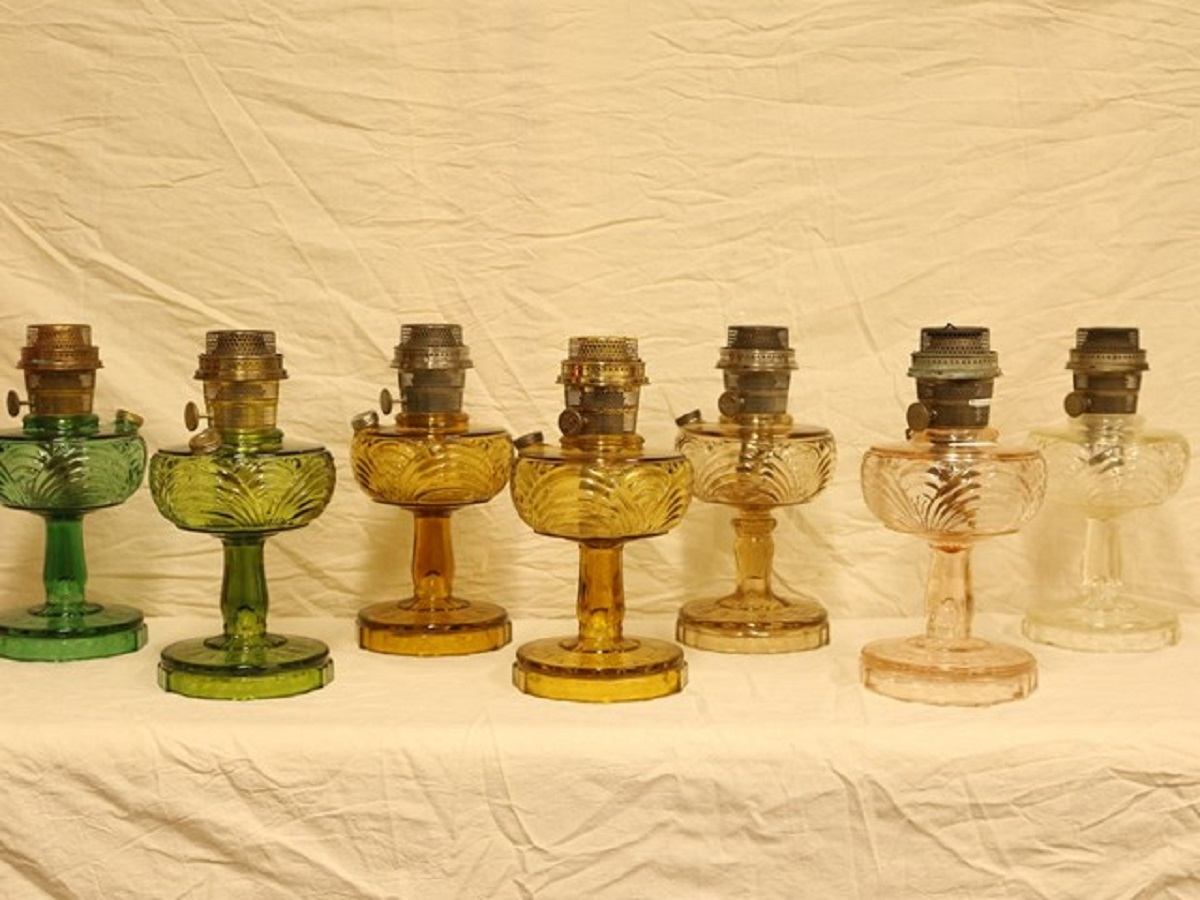 A display of colorful vintage oil lamps in green, blue, yellow and other shades.