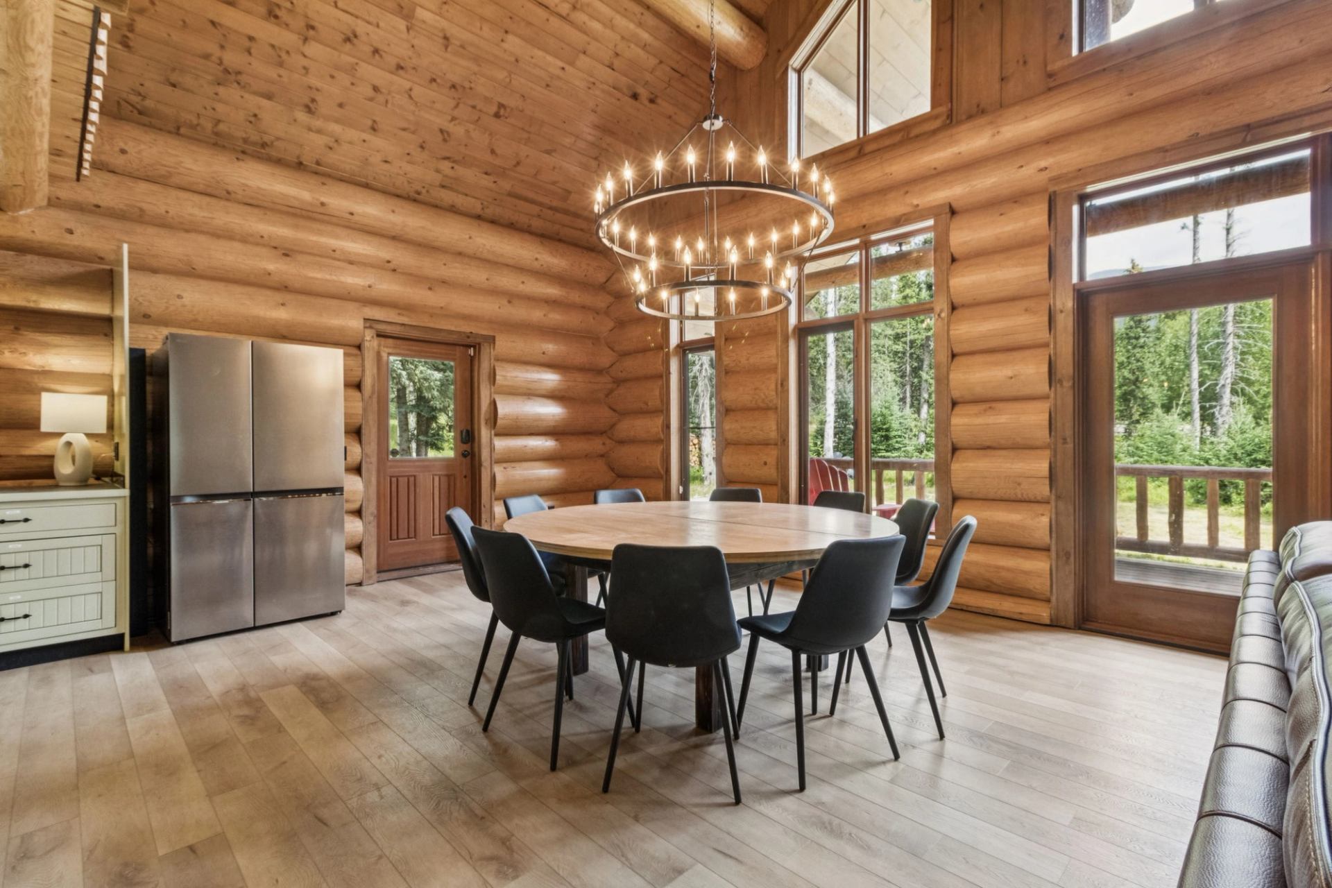 Log cabin dining area with round table, black chairs, and modern chandelier.