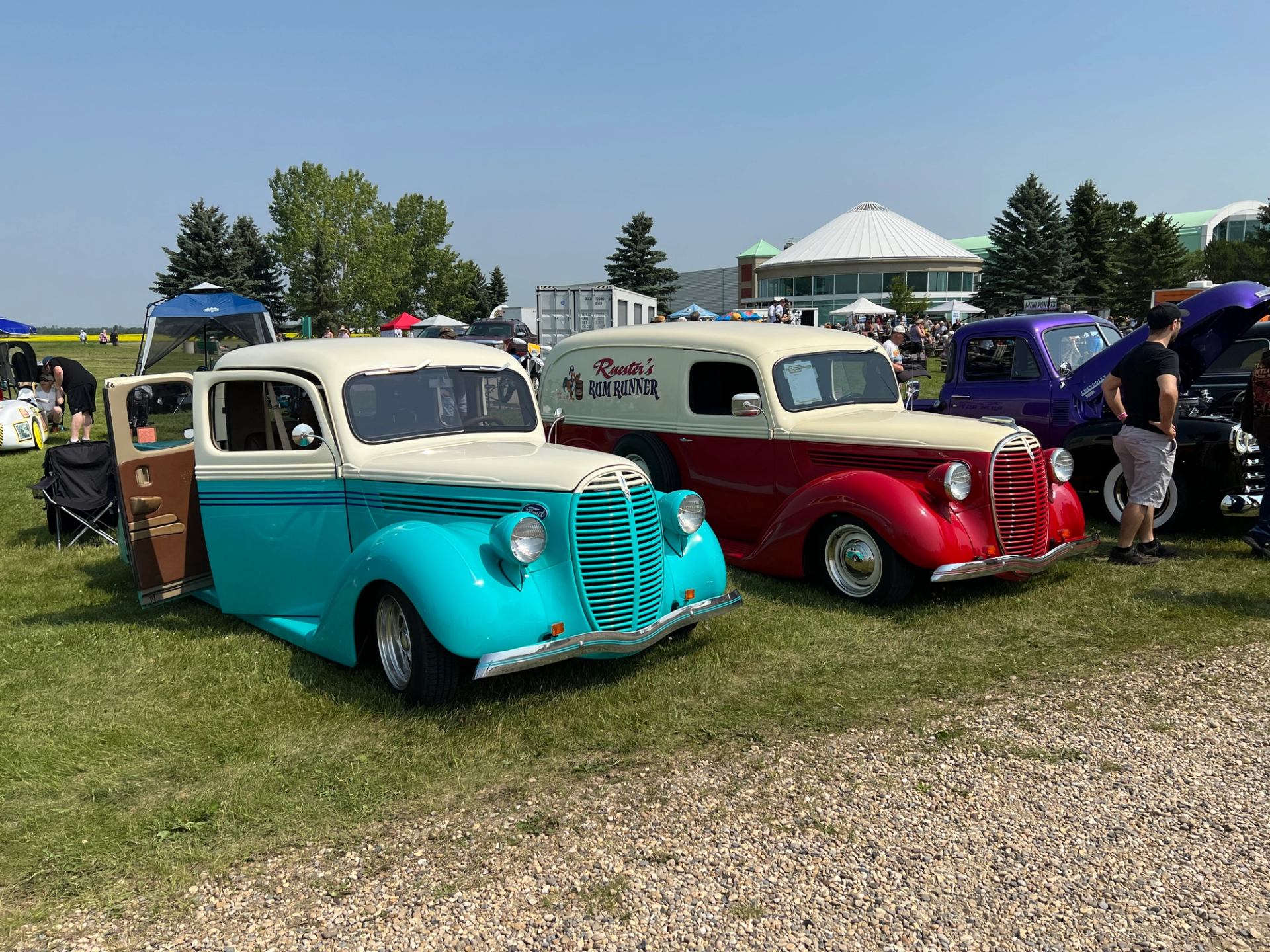 Two customized vintage cars in teal and red parked at a car show.