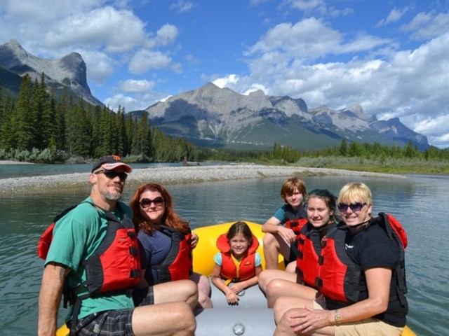 Rafting group on calm river with forest and mountain backdrop.