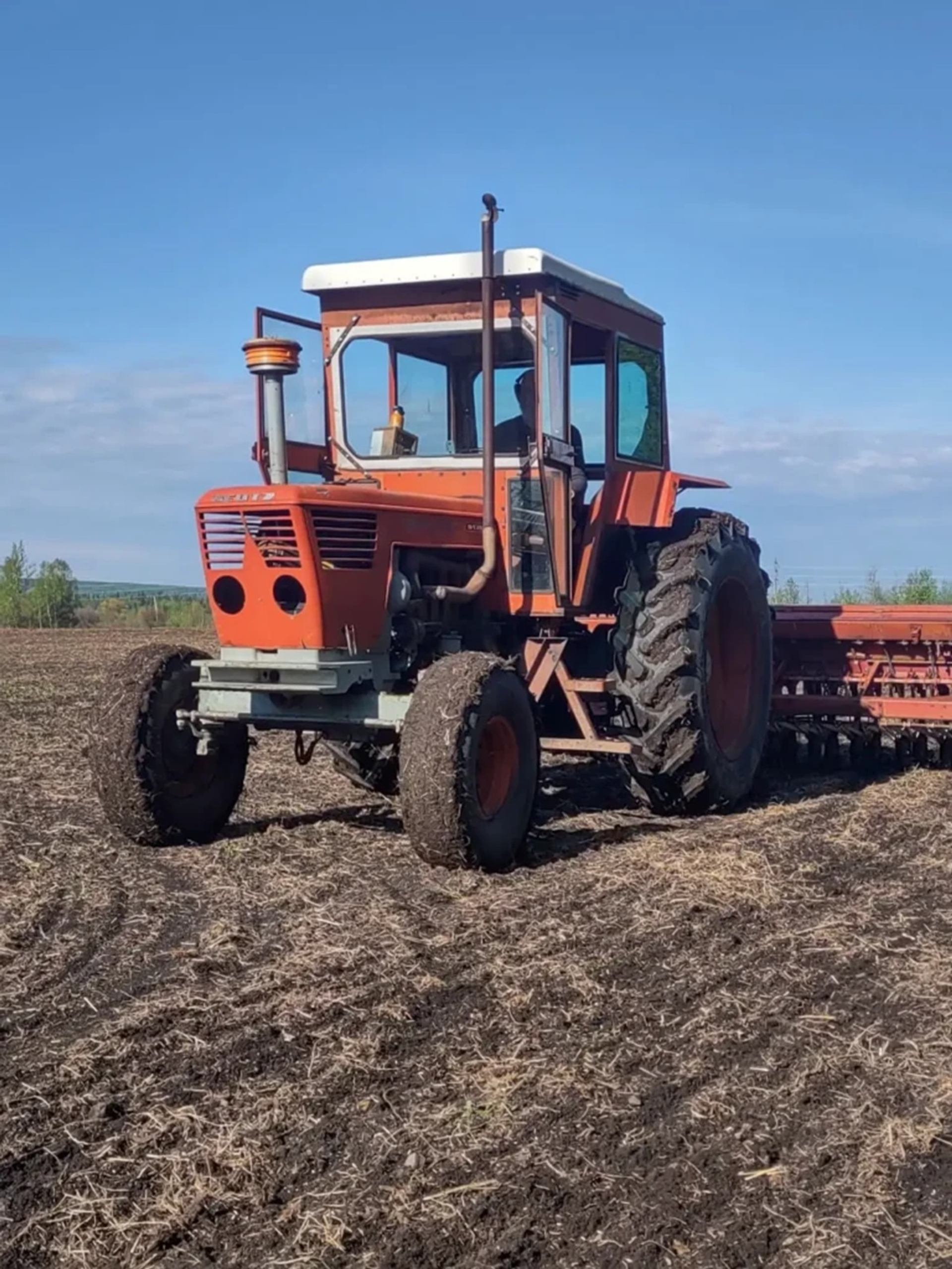 Orange tractor with cab pulls seeding equipment across a freshly tilled field.
