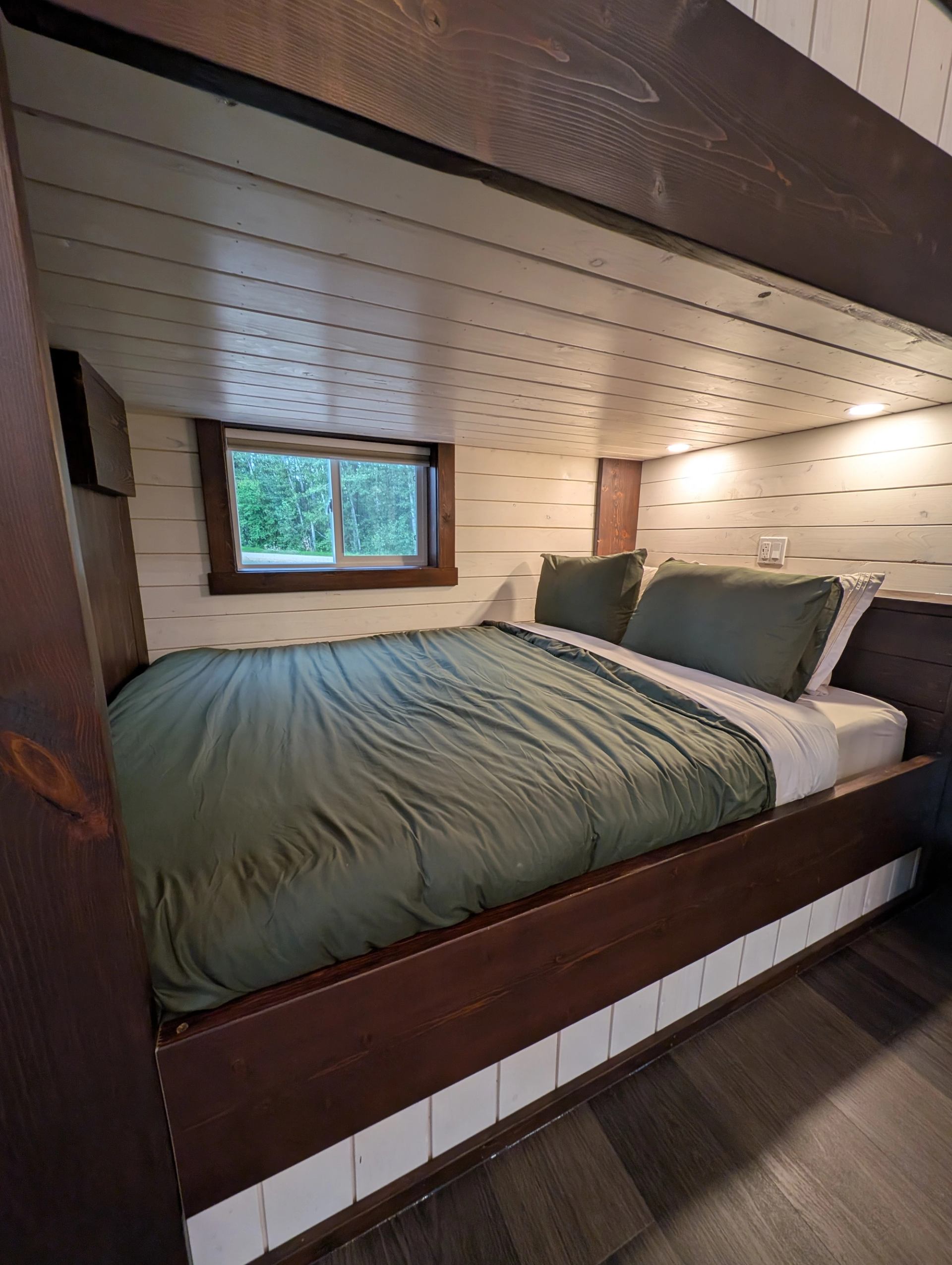 Built-in wooden bed with green bedding beneath a low plank ceiling.