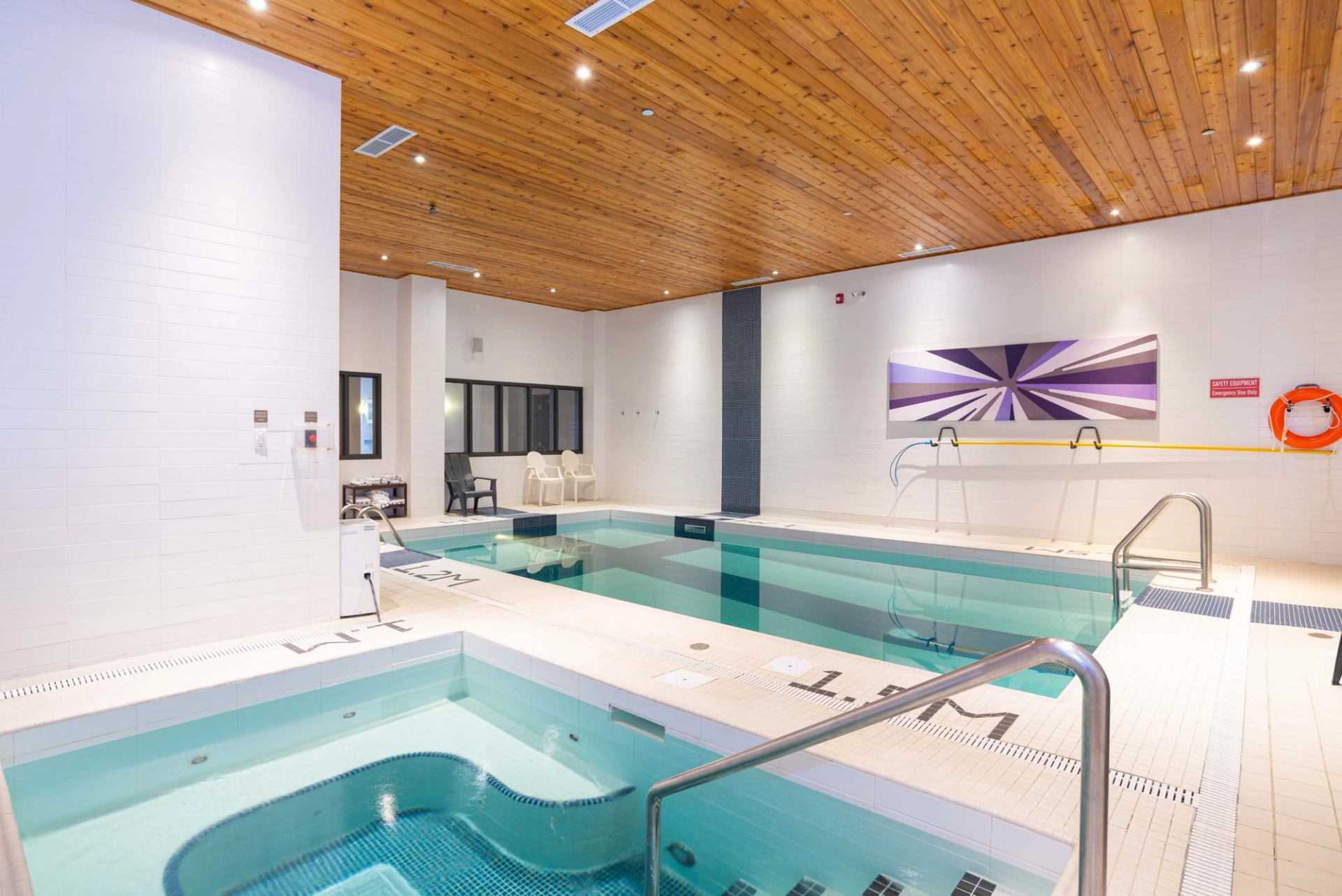 Indoor pool and hot tub area with wall art, seating, and safety rails.