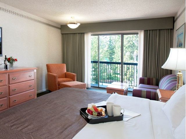 Hotel room with balcony doors, chairs, dresser, and table beside a bed.
