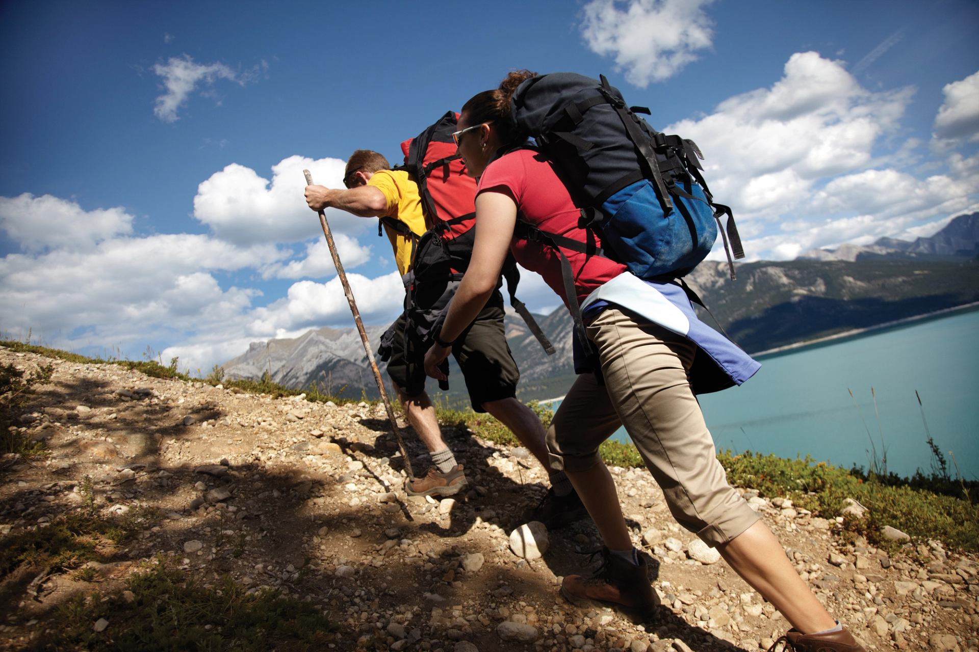 Two hikers climb a rocky trail overlooking a turquoise lake and mountain landscape at Paradise Valley.