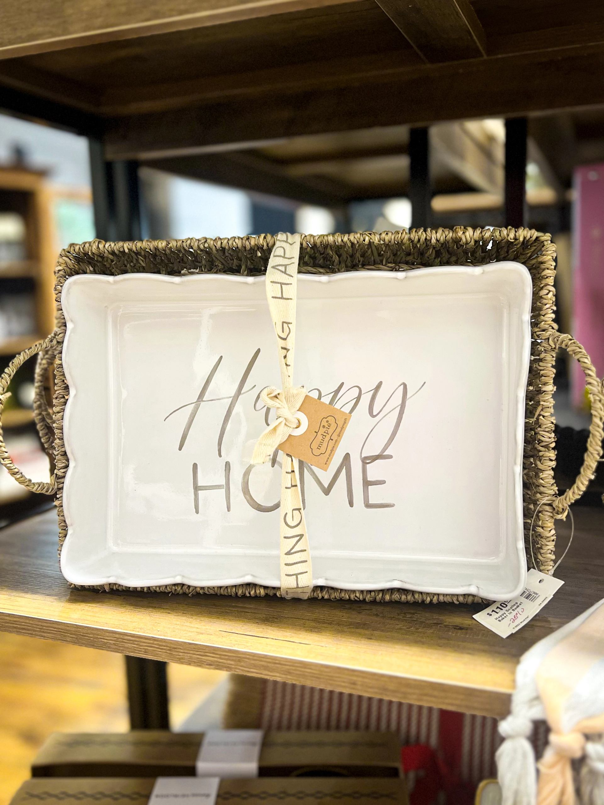White tray with “Home” lettering, displayed in woven basket on a wooden shelf.