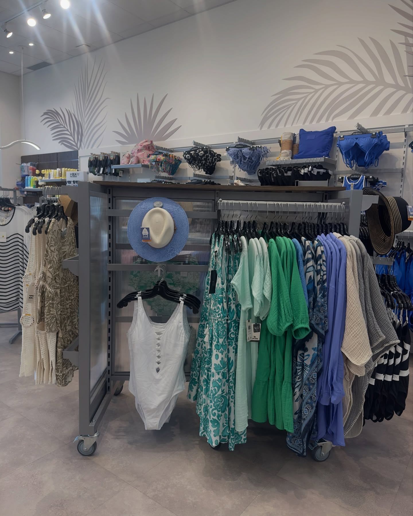 Clothing rack displays swimsuits, dresses, cover-ups and sun hats in a store.