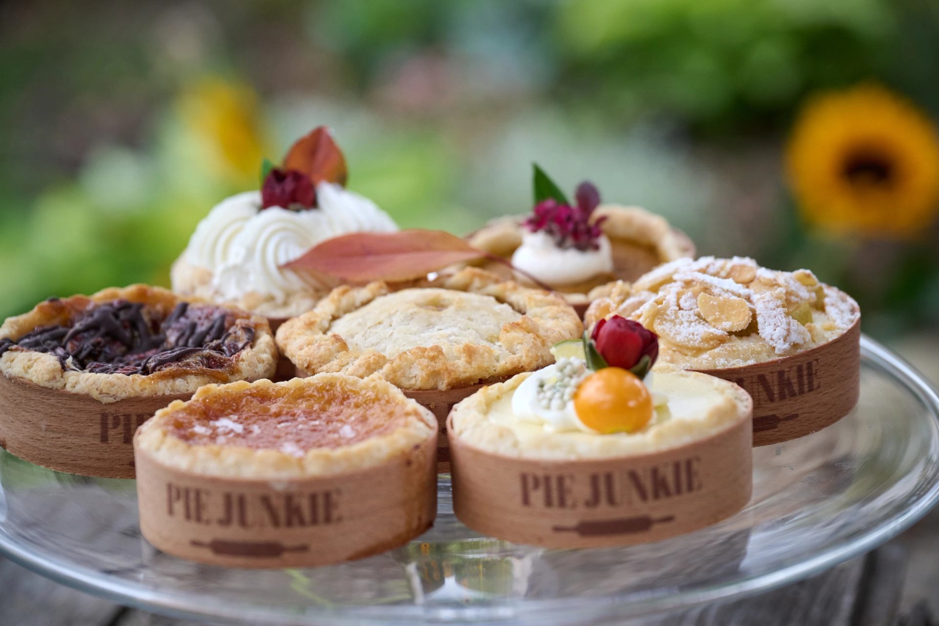 Assorted mini pies on a glass stand decorated with fruit and flowers.