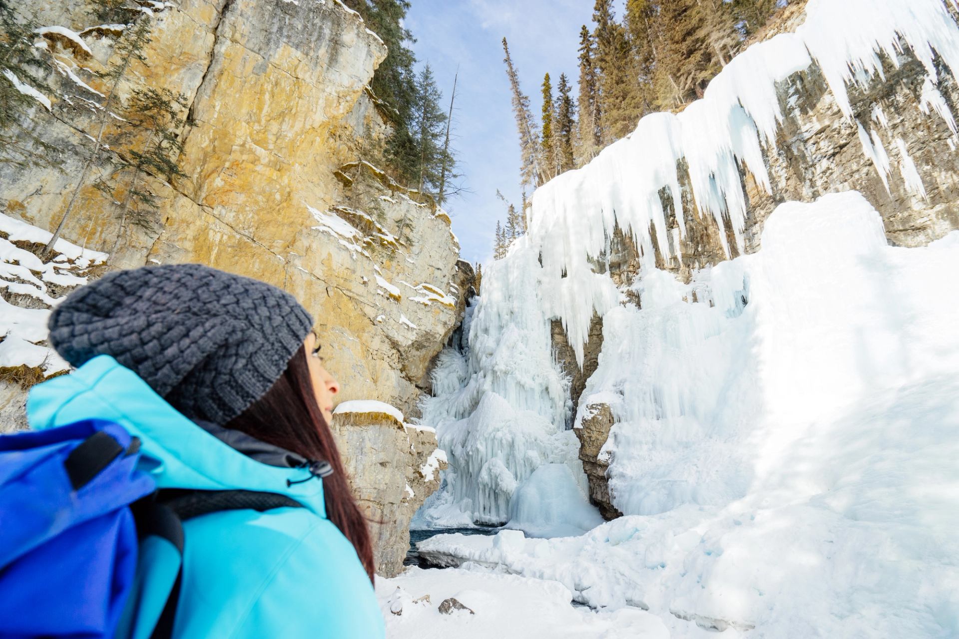 A hiker looks up at towering icy canyon walls and frozen formations.