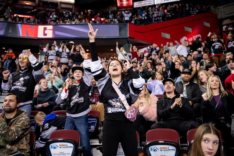 Packed indoor arena with cheering fans, raised hands, and scoreboard during Calgary Roughnecks game.