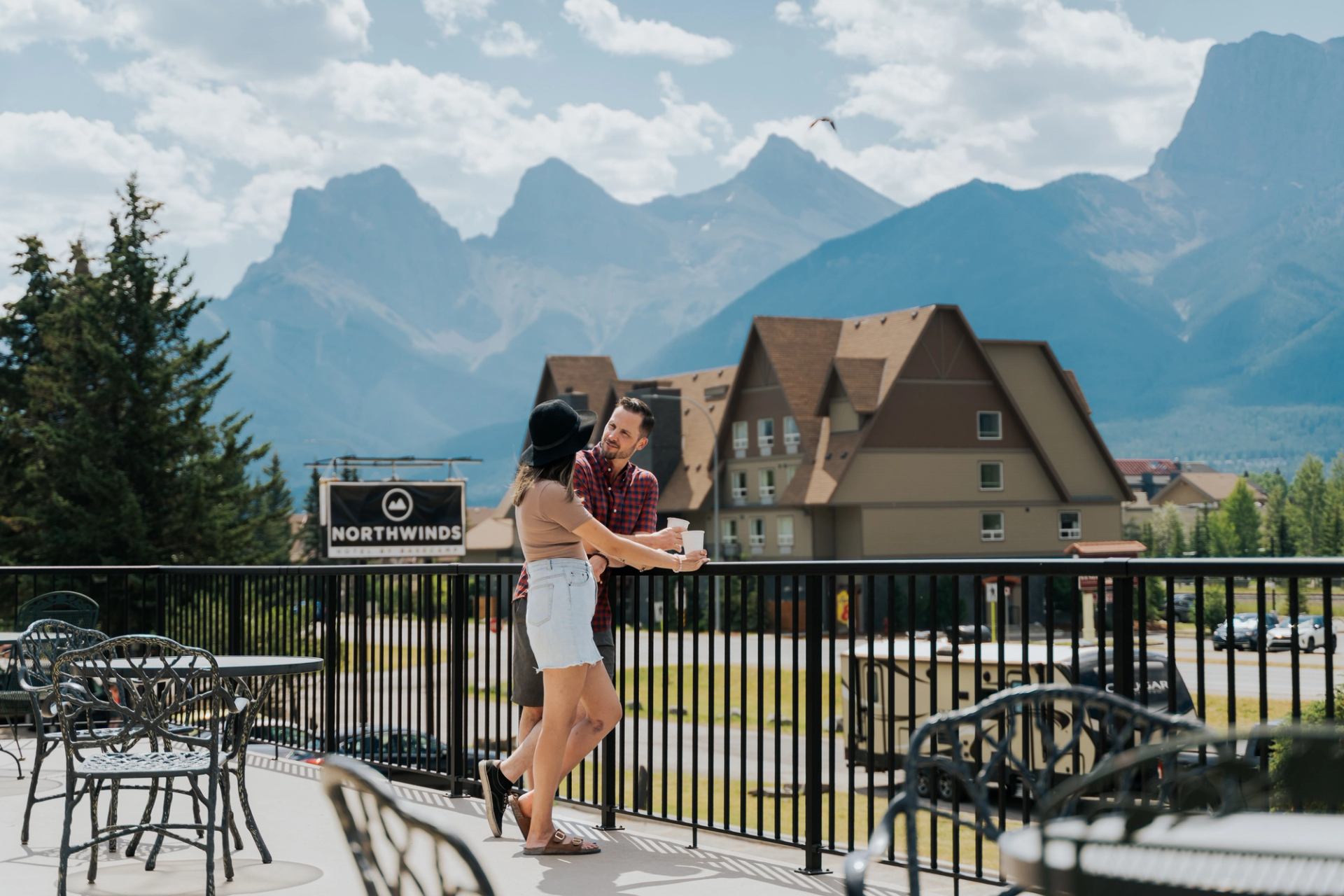 People holding coffee cups on a patio at Northwinds, with mountains and buildings behind..