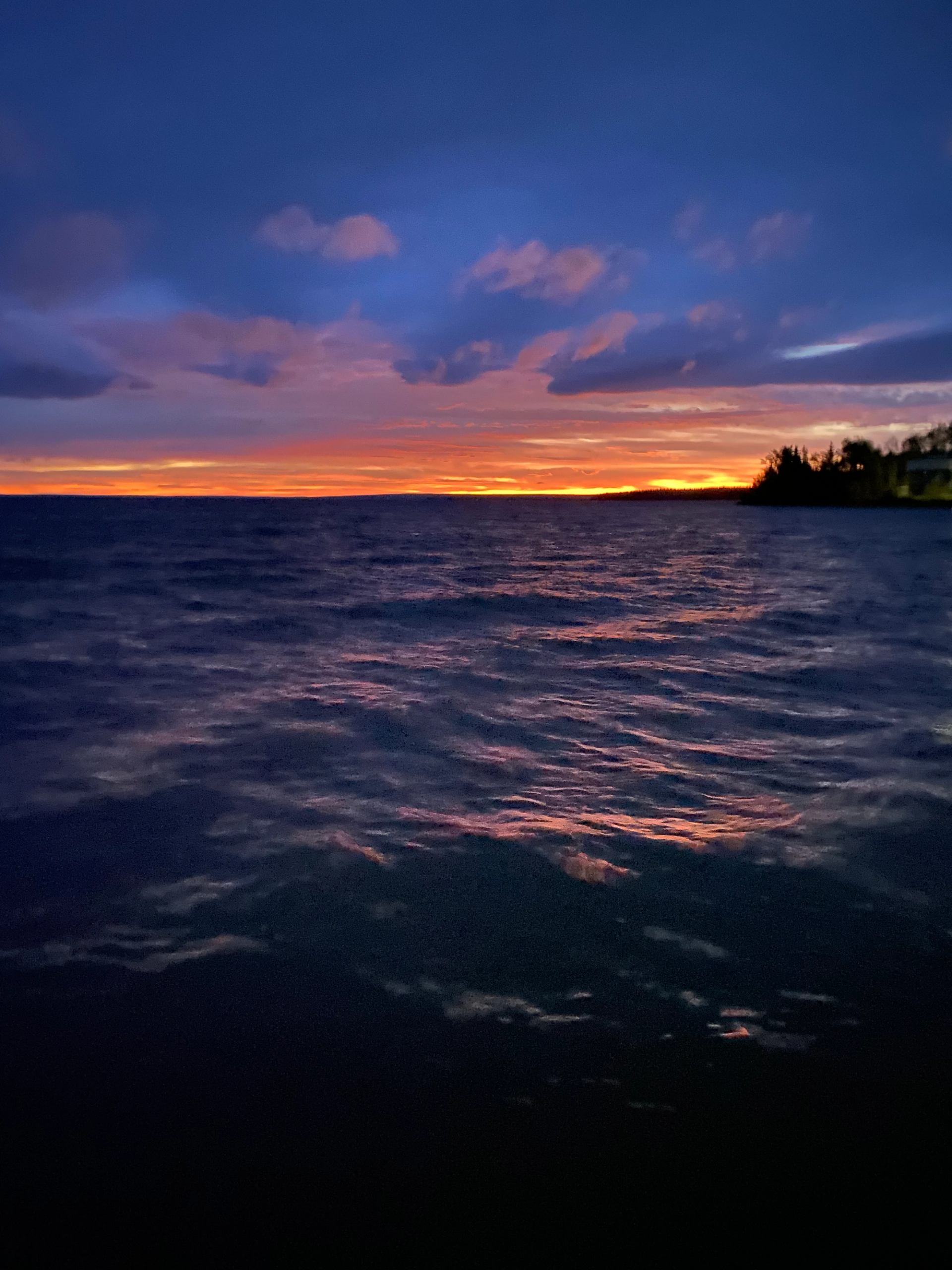 Vibrant sunset casting warm light over rippling water and a distant treeline.